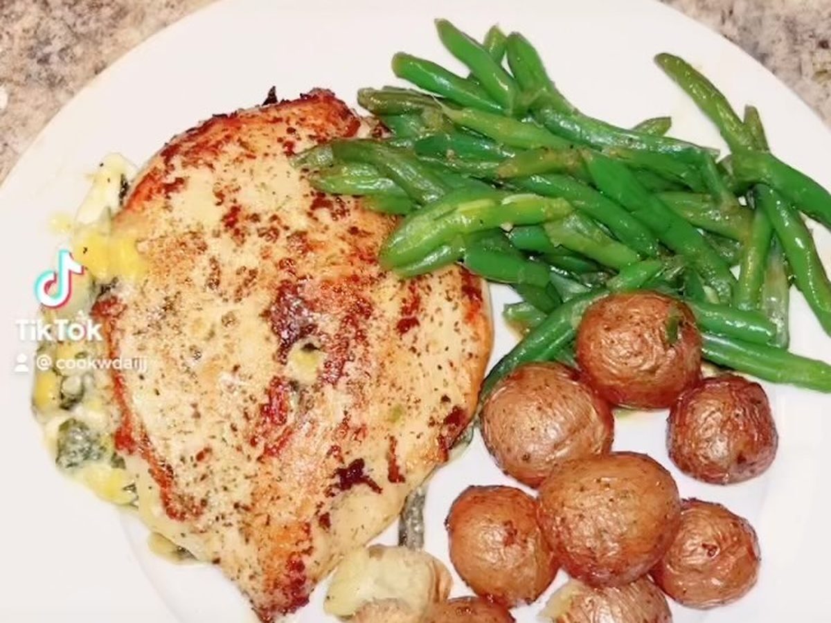A seared chicken breast with green beans and roasted baby potatoes on a white plate