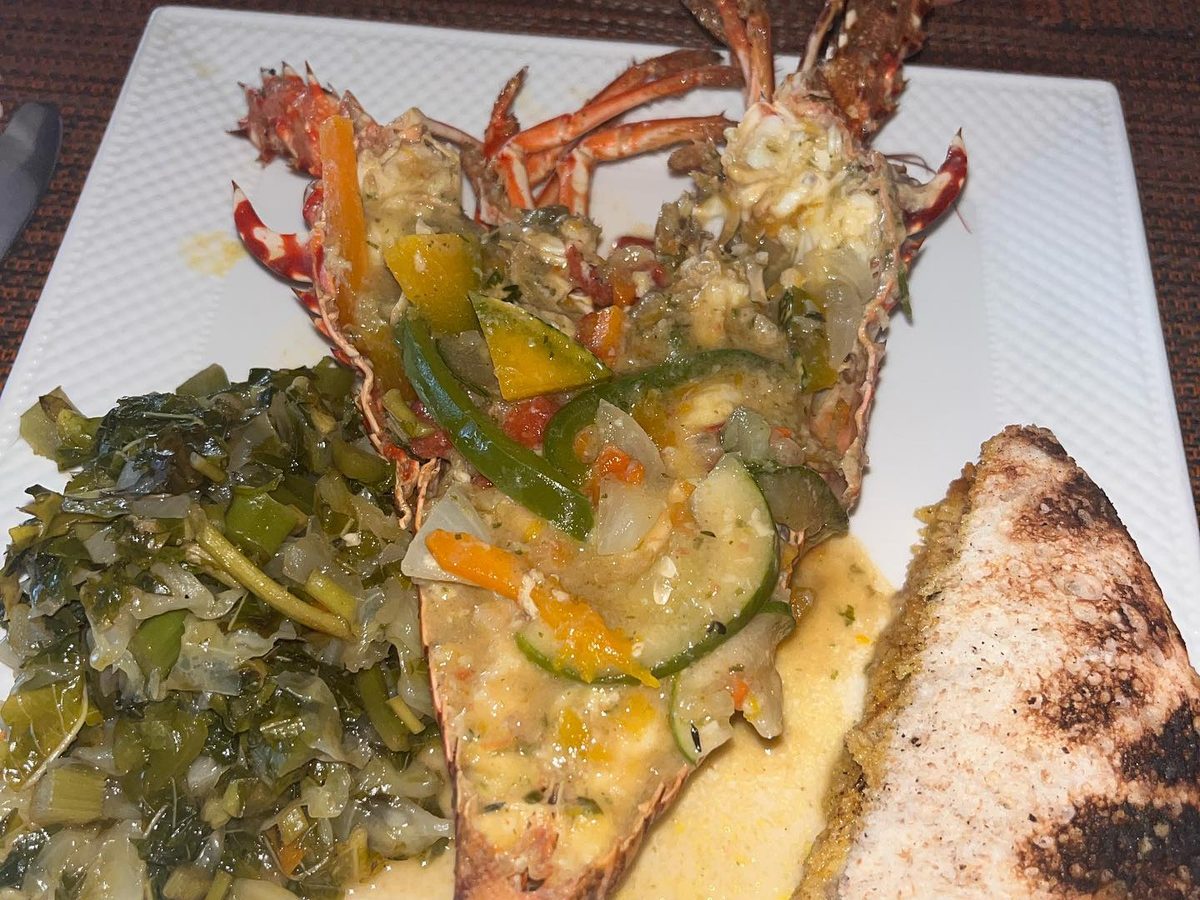 A split grilled lobster tail over grits with peppers, collard greens and grilled bread
