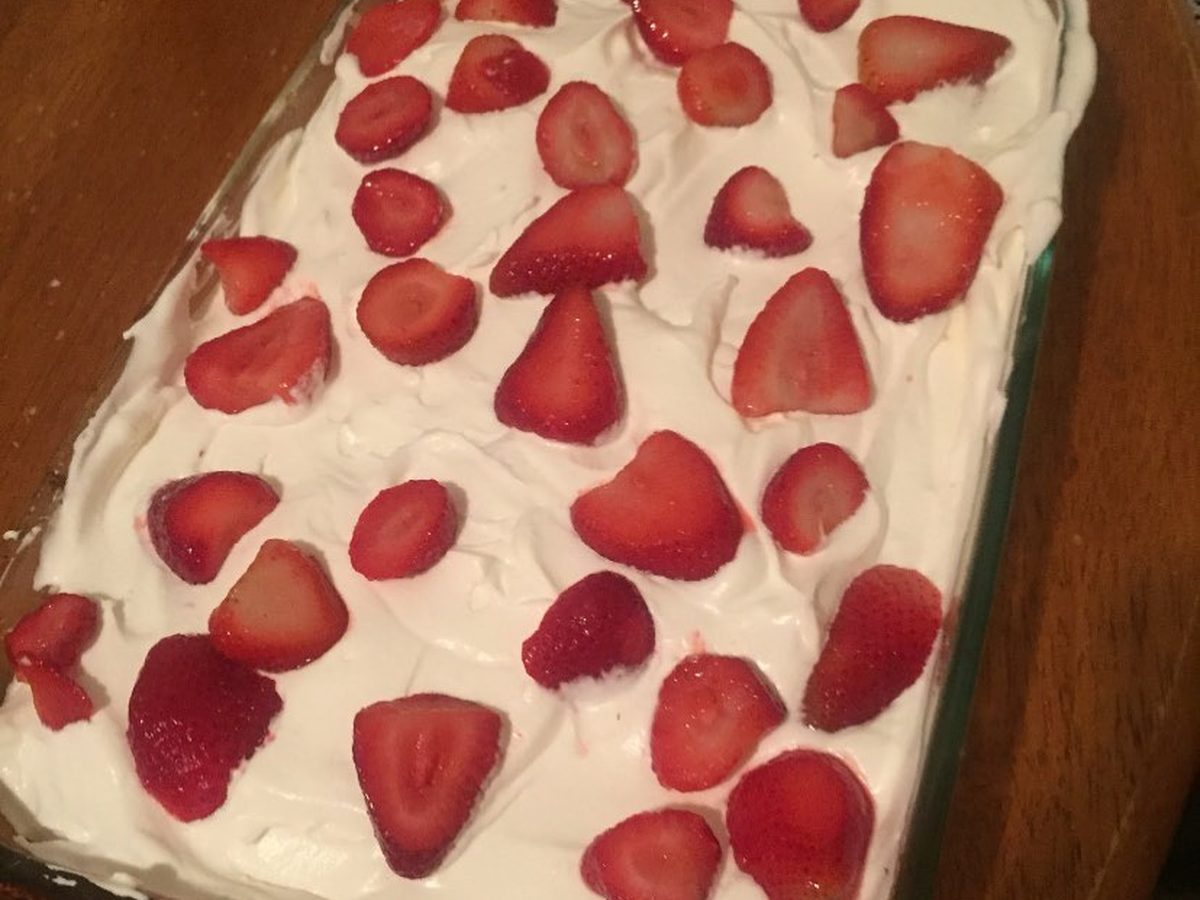 A tray of tres leches cake with whipped cream and sliced strawberries on top