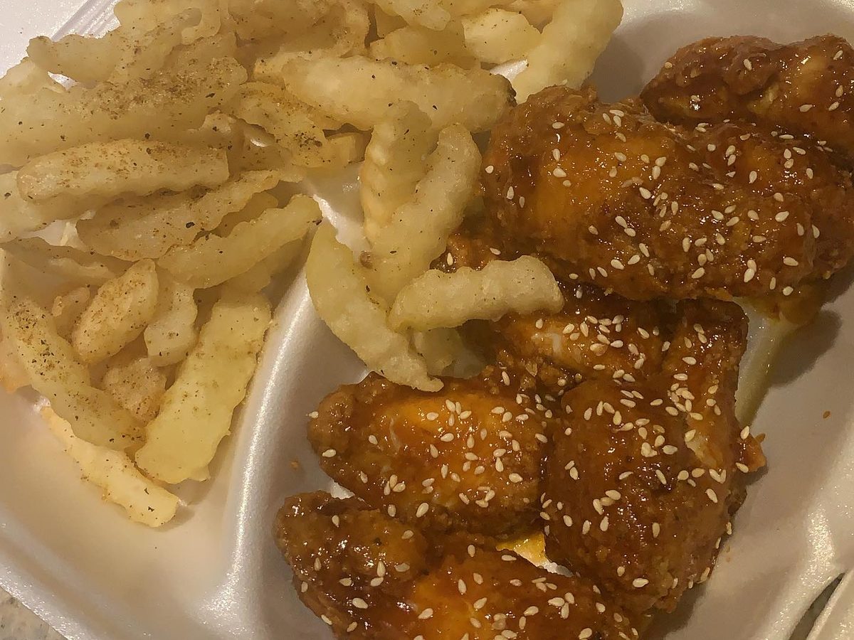 Sweet Thai chili glazed wings with sesame seeds beside crinkle-cut fries in a takeout container